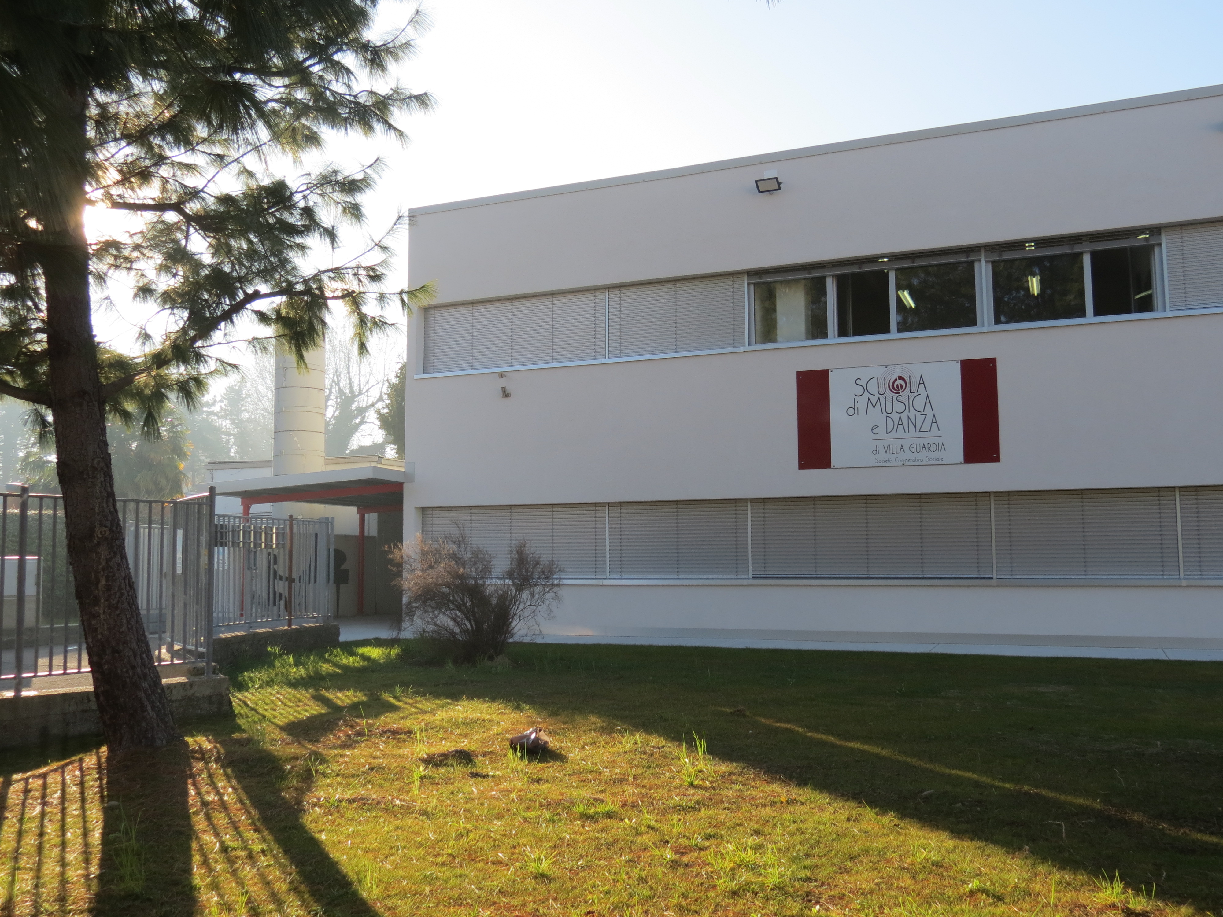 Facciata della Scuola di Musica di Maccio a Villa Guardia, con erba verde e alberi che si affacciano sul lato.