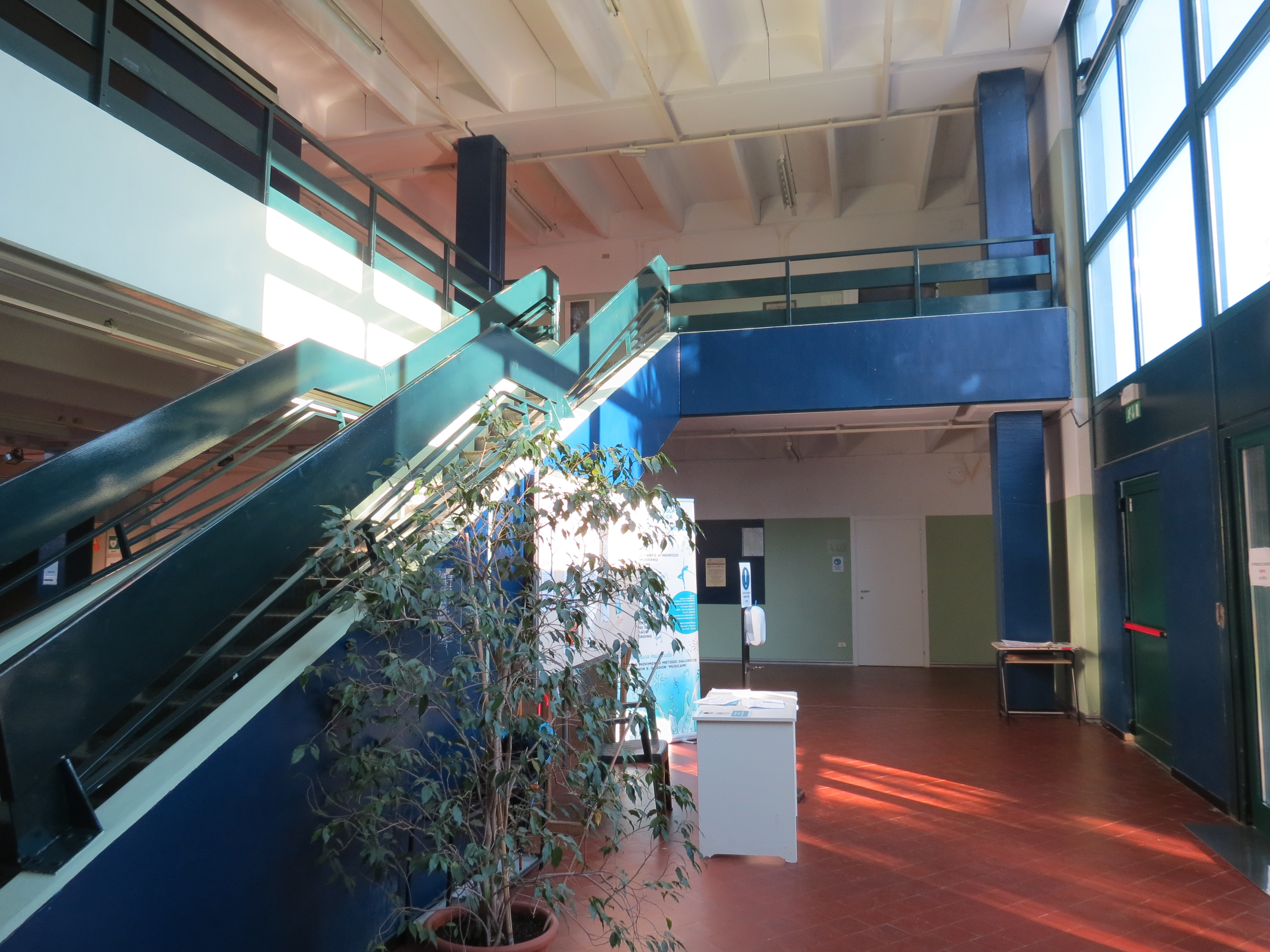 Interno della Scuola di Musica di Maccio, con una scala e una pianta decorativa visibili.