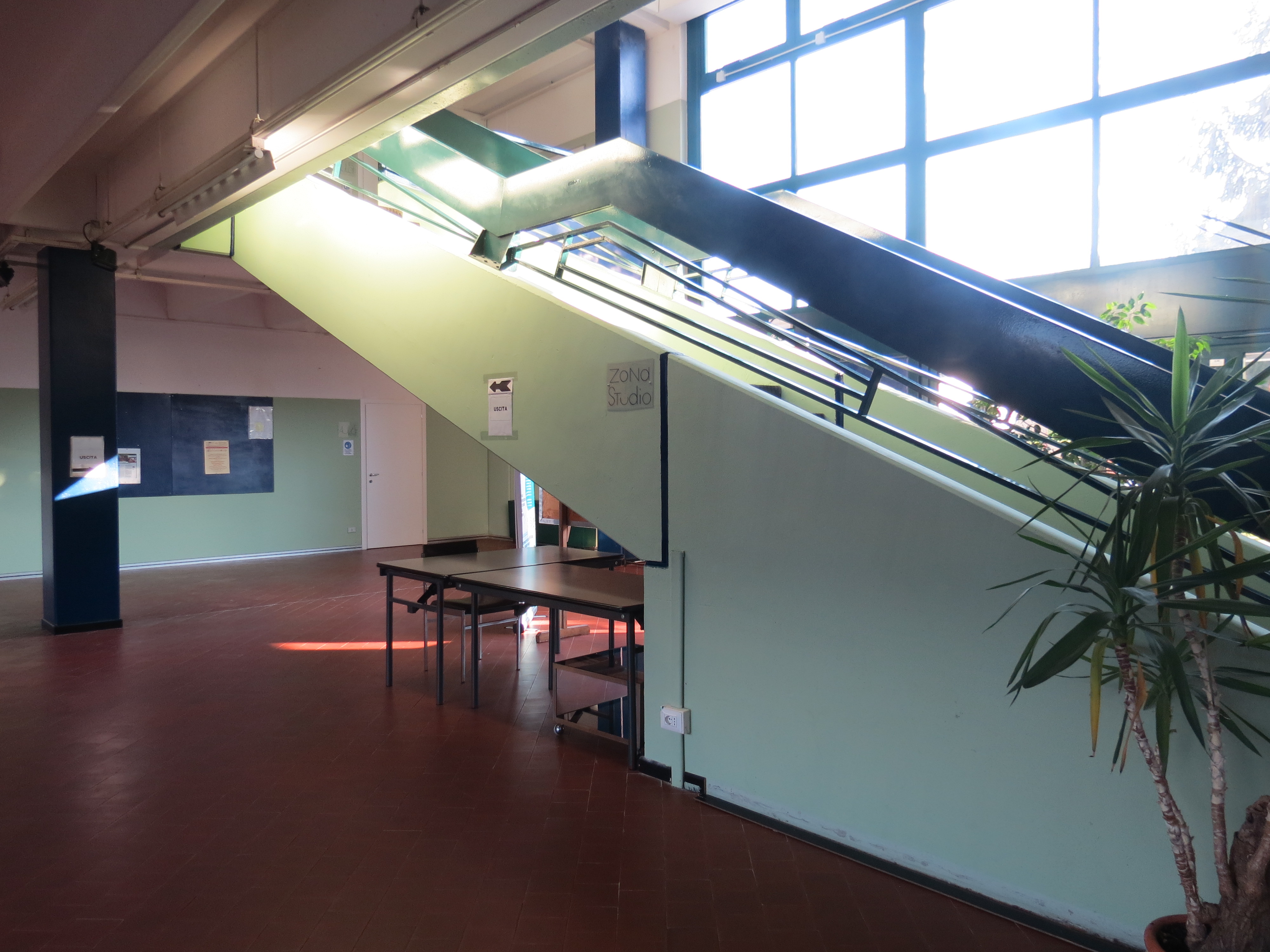 Interno della Scuola di Musica di Maccio, con scale, tavoli e grandi finestre che illuminano lo spazio.
