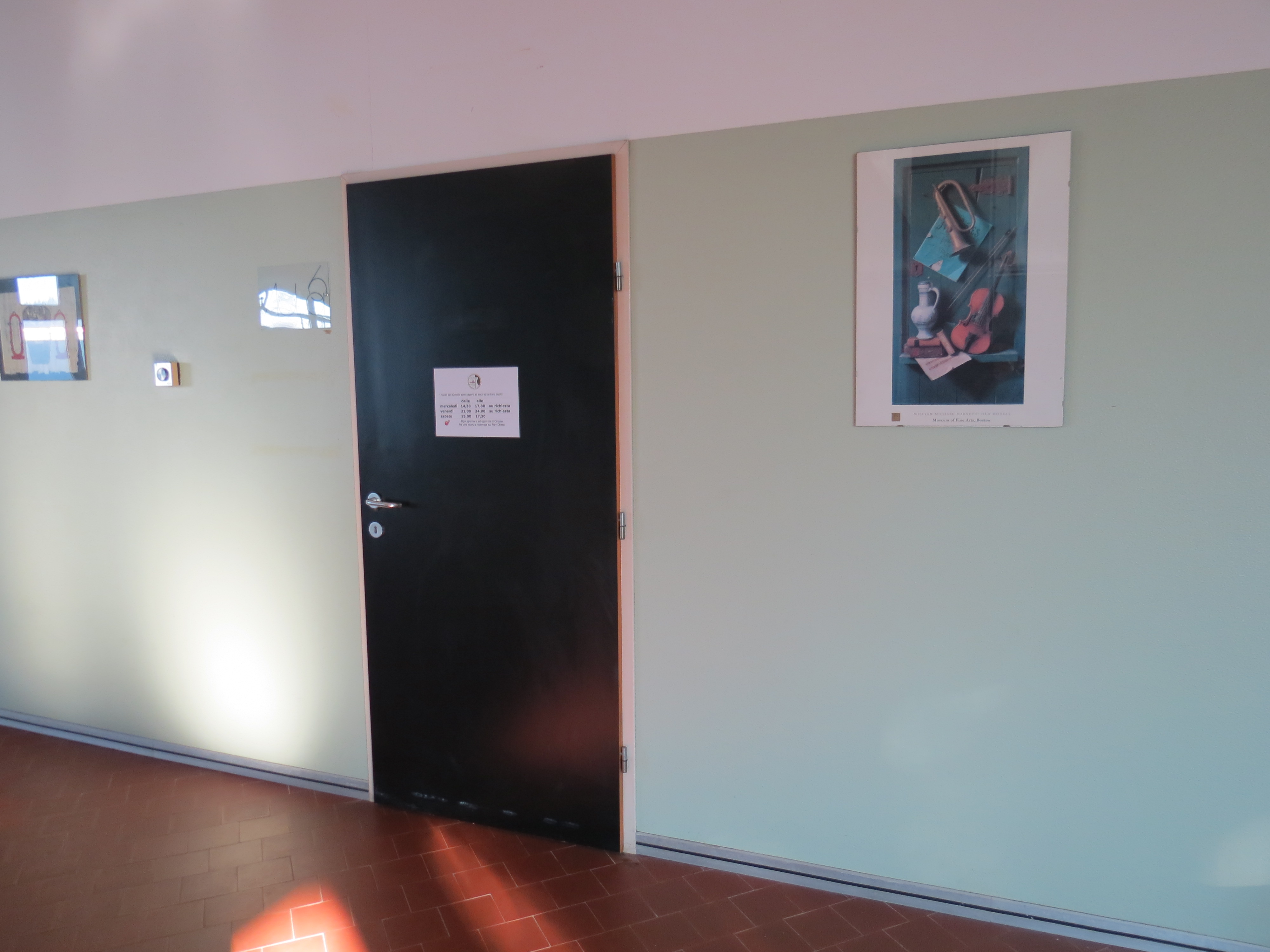 Entering the Scuola di Musica di Maccio, showcasing a black door on a green wall with an art piece nearby.