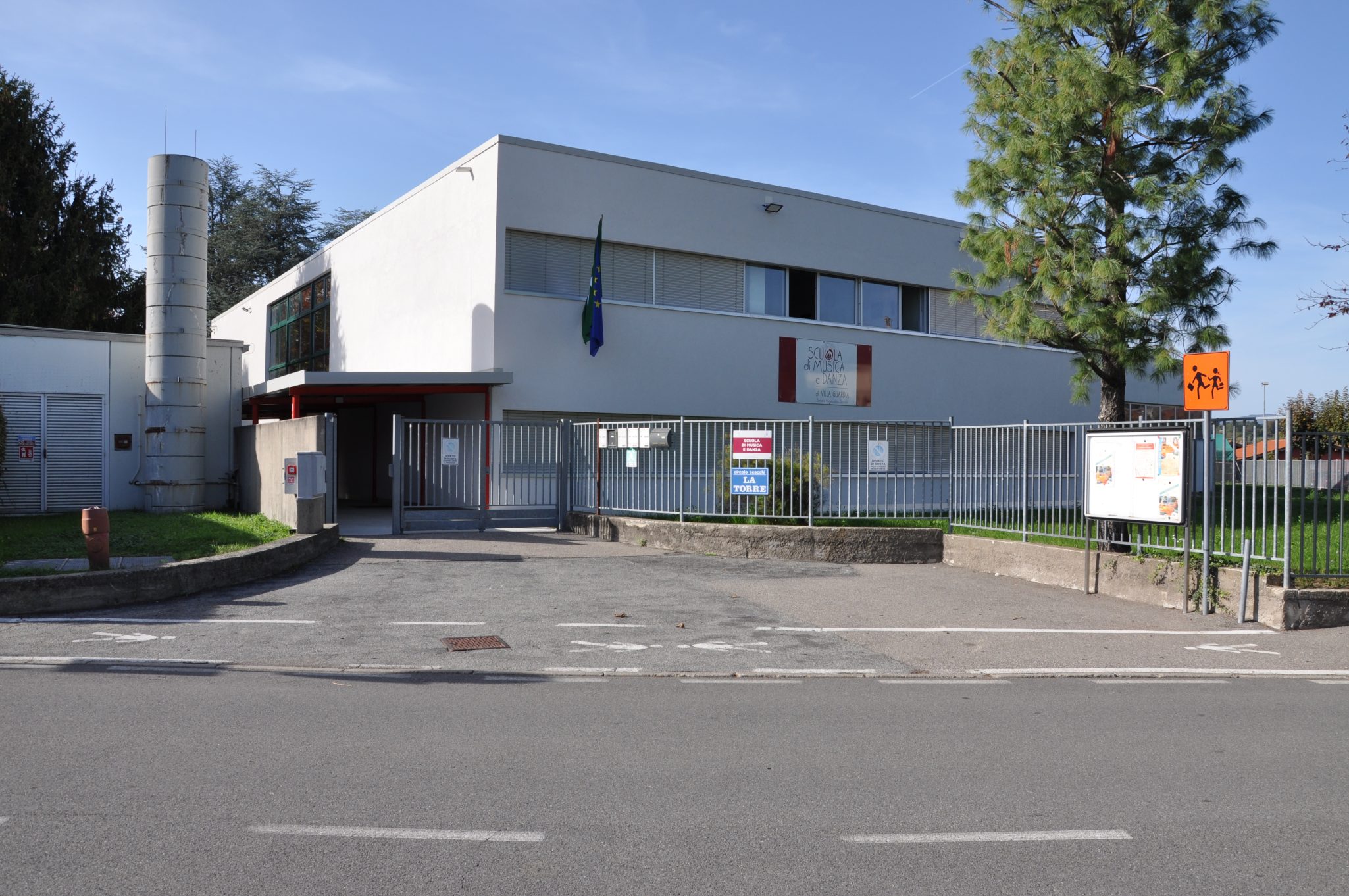 Facciata della Scuola di Musica di Maccio a Villa Guardia, con un cancello e un albero sul lato destro.