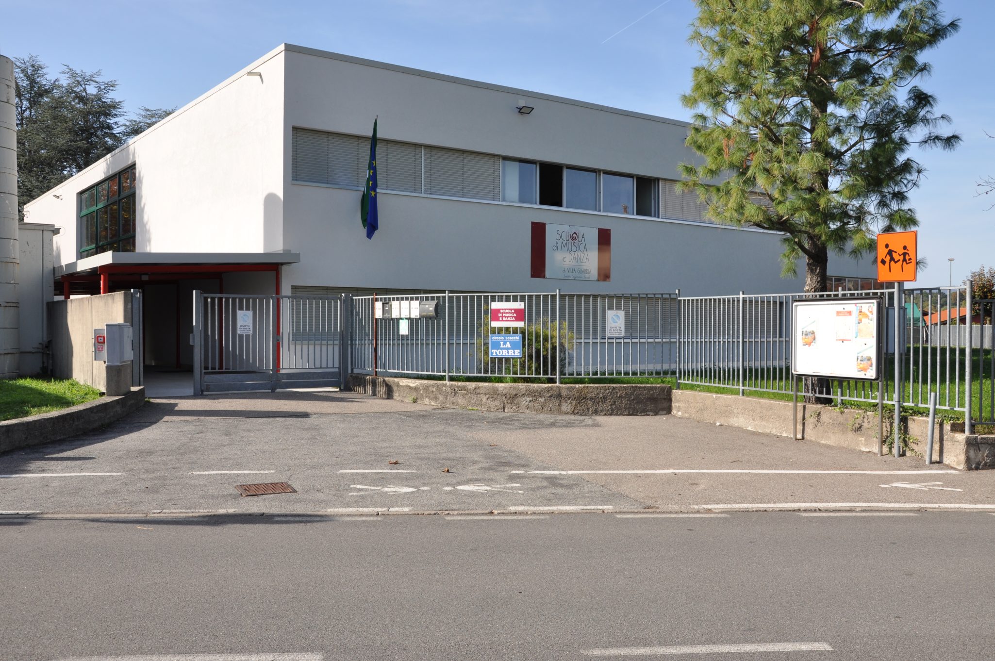 Facciata della Scuola di Musica di Maccio a Villa Guardia con recinzione e strada in primo piano.