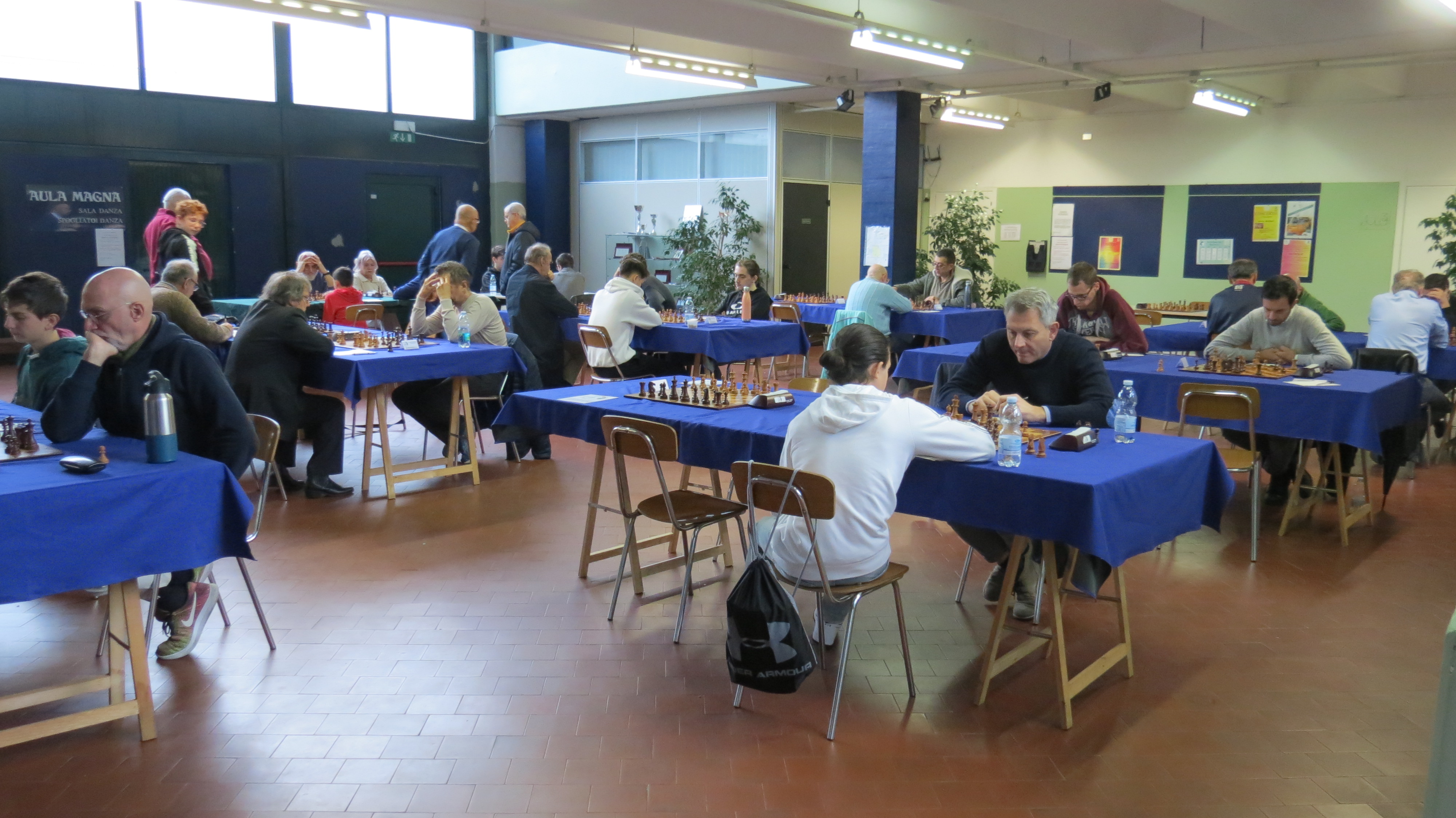 Sala di gioco del torneo di scacchi con tavoli blu, giocatori concentrati e pezzi di scacchi disposti su ciascun tavolo.
