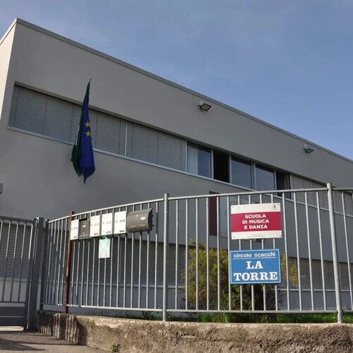 Facciata di una scuola con bandiera, recinzione e cartelli informativi.
