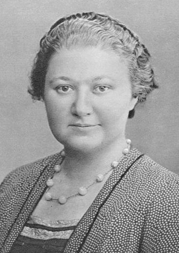 Ritratto di una campionessa di scacchi del XX secolo, con i capelli raccolti e un abbigliamento elegante, che indossa una collana di perle.