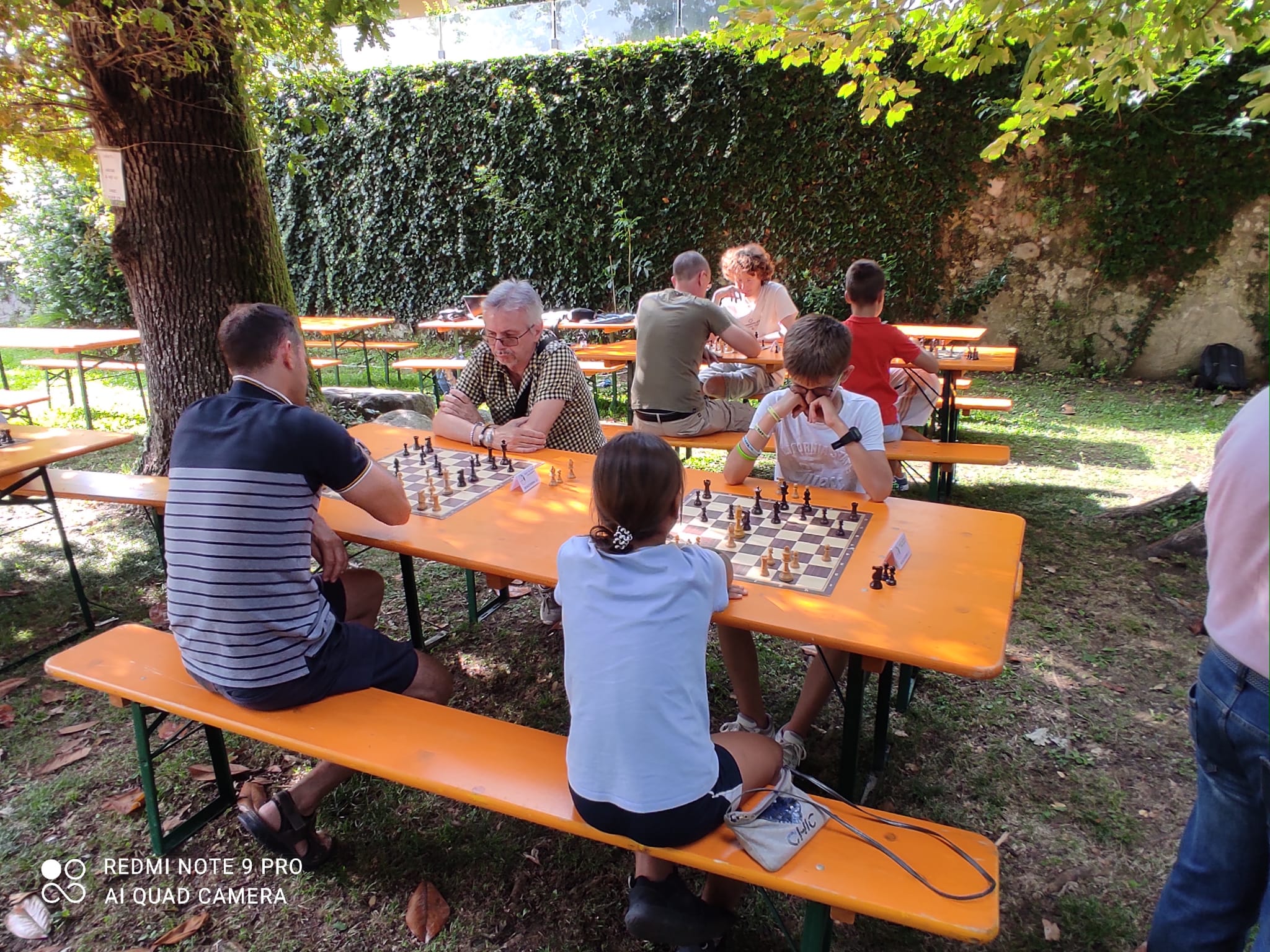 Giocatori di scacchi si cimentano in una partita all'aperto, seduti a tavoli di legno nel Parco Comunale durante il Torneo di Casnate con Bernate.