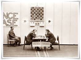 Bobby Fischer e Mark Taimanov durante il torneo dei candidati del 1971, seduti davanti a una scacchiera con un grande orologio di scacchi visibile sullo sfondo.