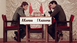 Garry Kasparov e Anatoly Karpov durante una partita di scacchi, seduti di fronte a un tavolo con le bandiere russe e cinesi.