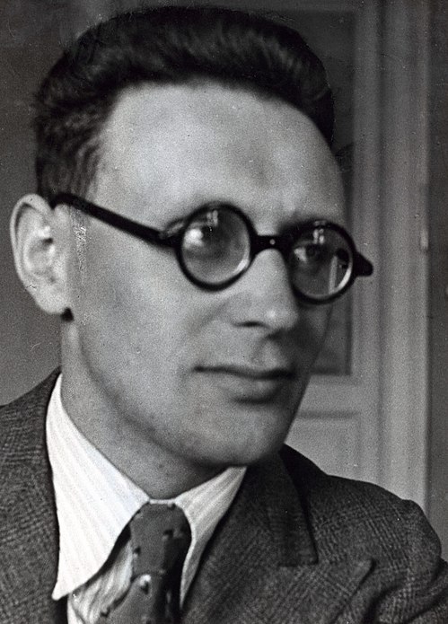 Ritratto in bianco e nero di un uomo con occhiali tondi e giacca elegante, che guarda verso destra con un'espressione seria.