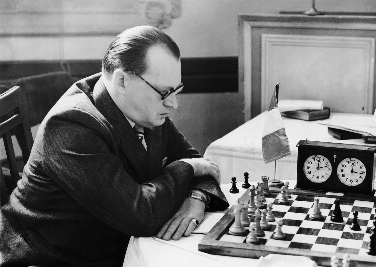 Un giocatore di scacchi concentrato mentre analizza una posizione sulla scacchiera, con una bandiera dietro di lui e un orologio da scacchi accanto.