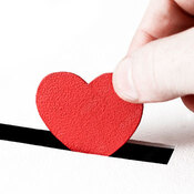 A person's hand placing a red heart shape into a slot.