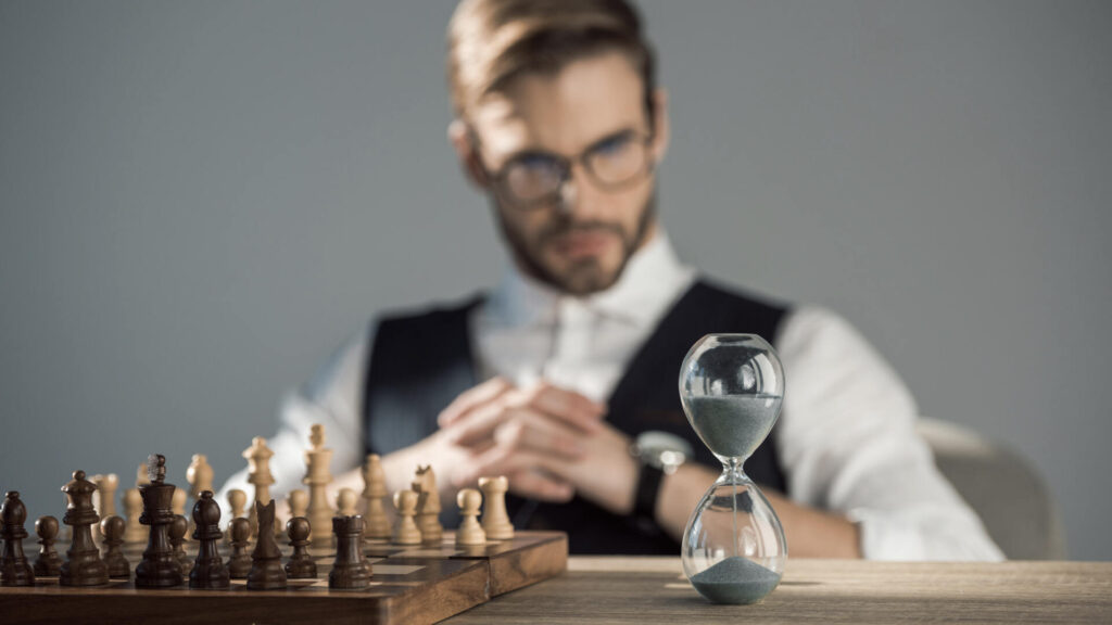 Un giocatore di scacchi concentrato osserva la scacchiera mentre una clessidra segna il tempo di gioco.
