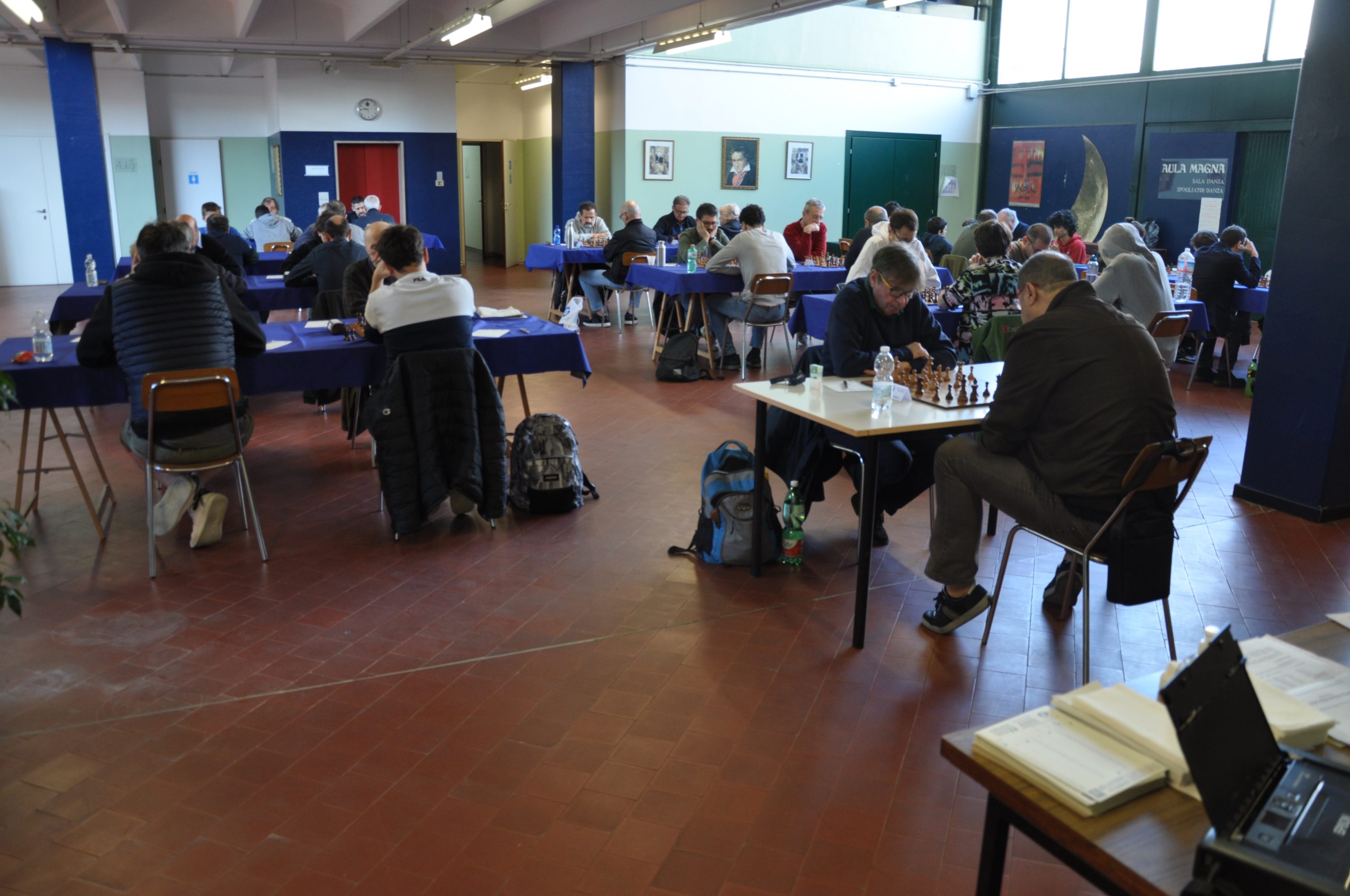 A chess tournament in progress, showcasing several players engaged at tables in a spacious room with blue and white decor.