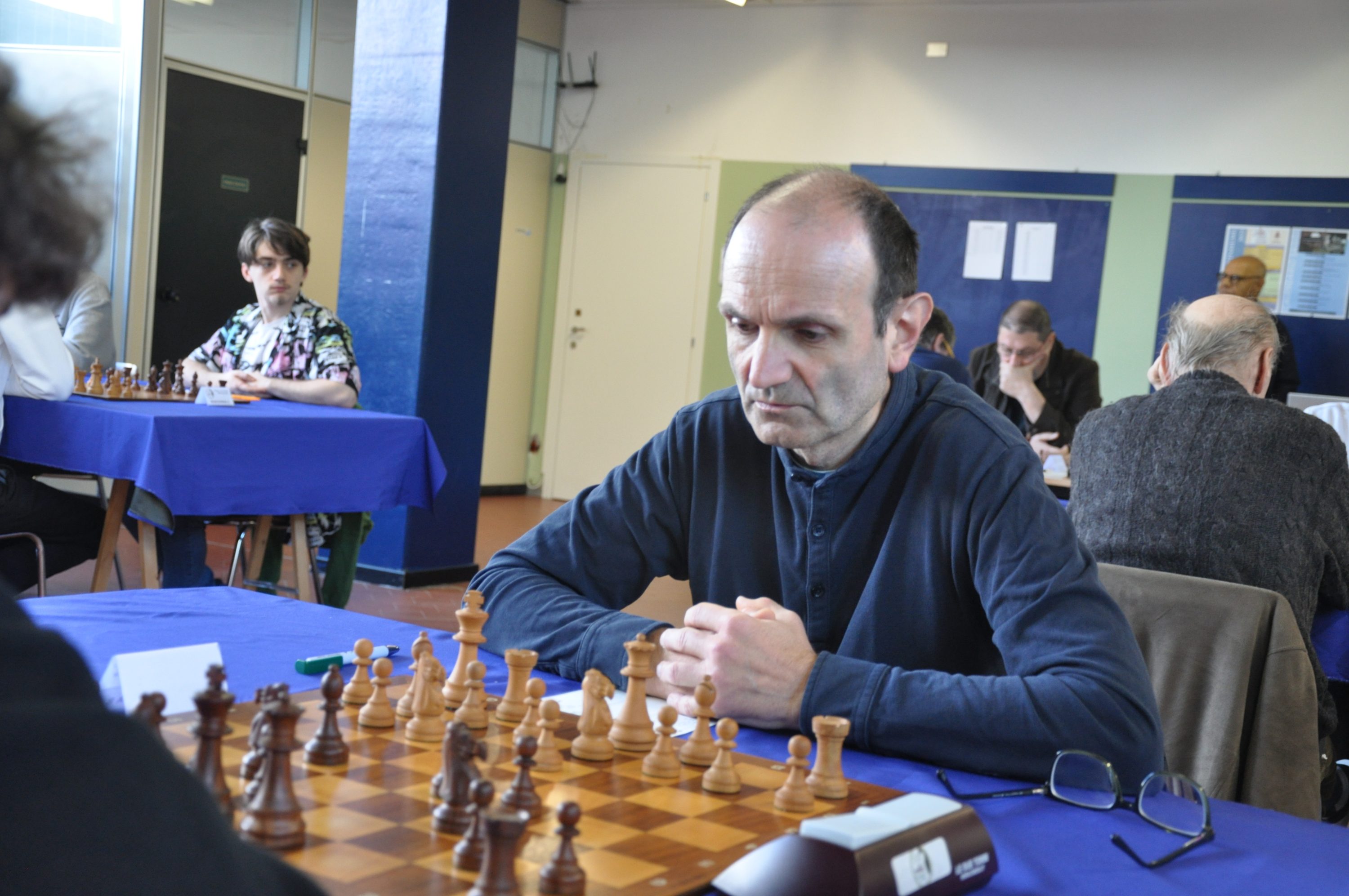 A chess player focused on the board, surrounded by other players in a tournament setting.