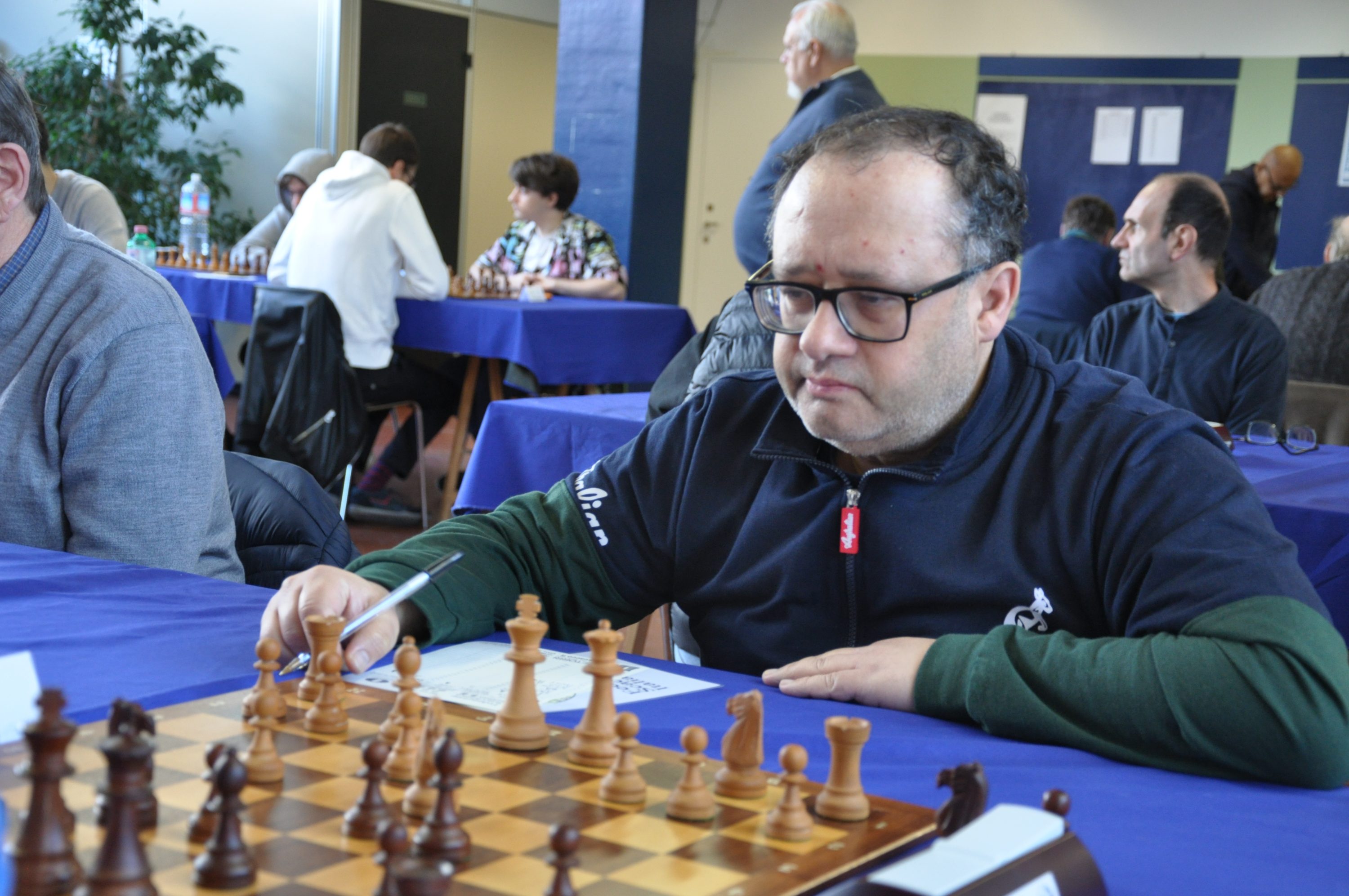 A chess player intently focusing on the game, with a chessboard and pieces in front of him.
