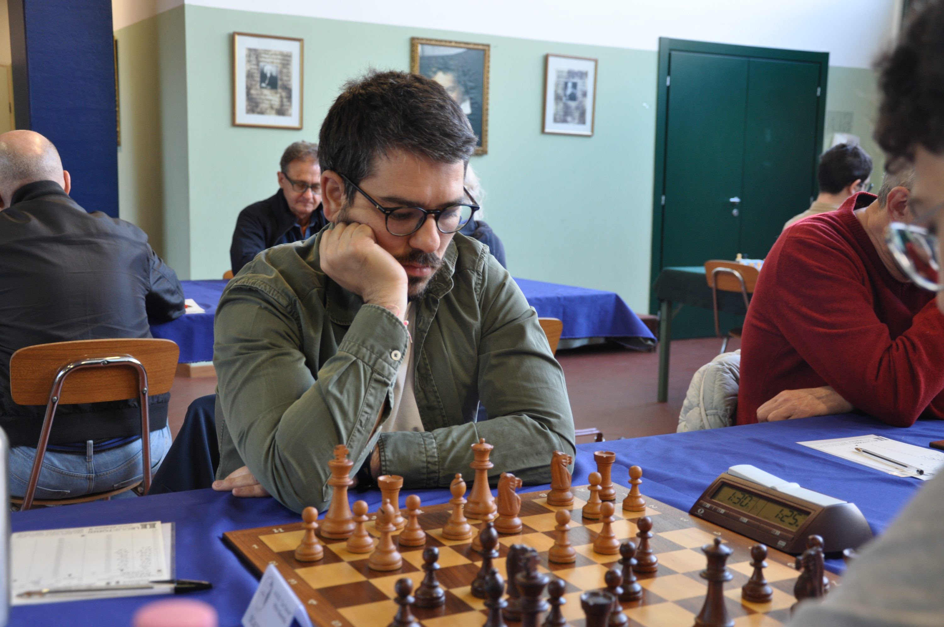 A focused chess player deep in thought during a game, with a chessboard in front and other players visible in the background.