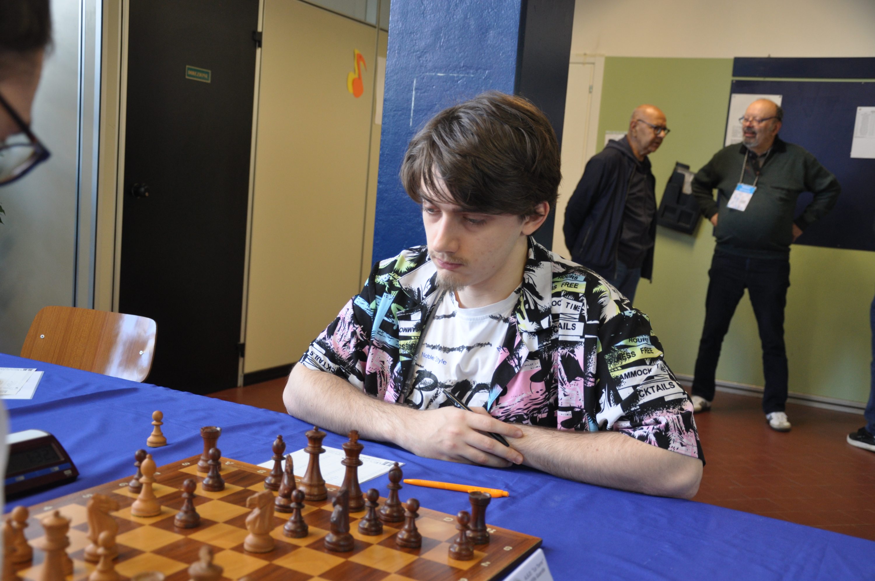 Un jugador de ajedrez enfocado frente a un tablero en una competencia, con espectadores al fondo.