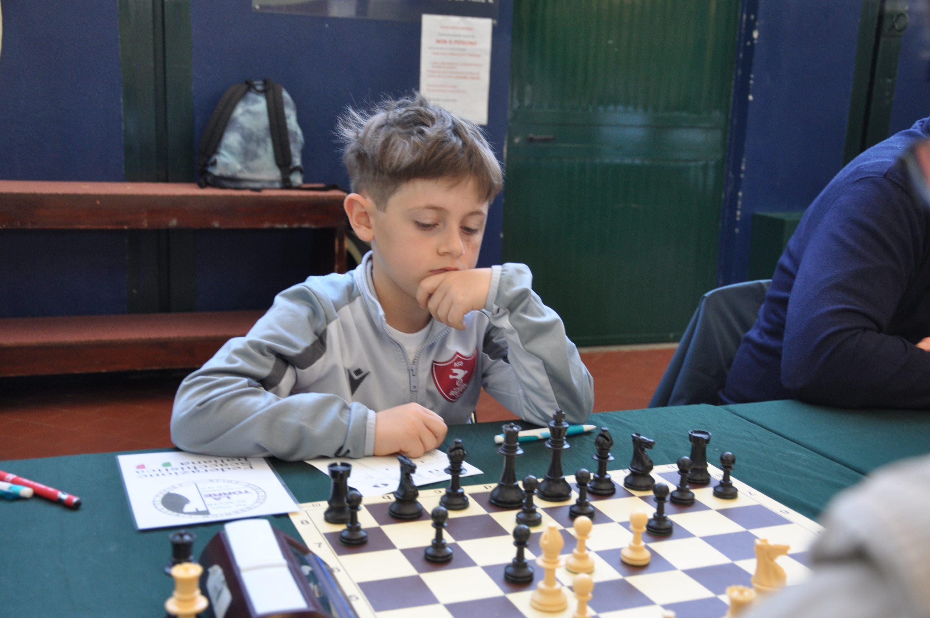 A young boy thoughtfully contemplating his next move while playing chess on a green table.