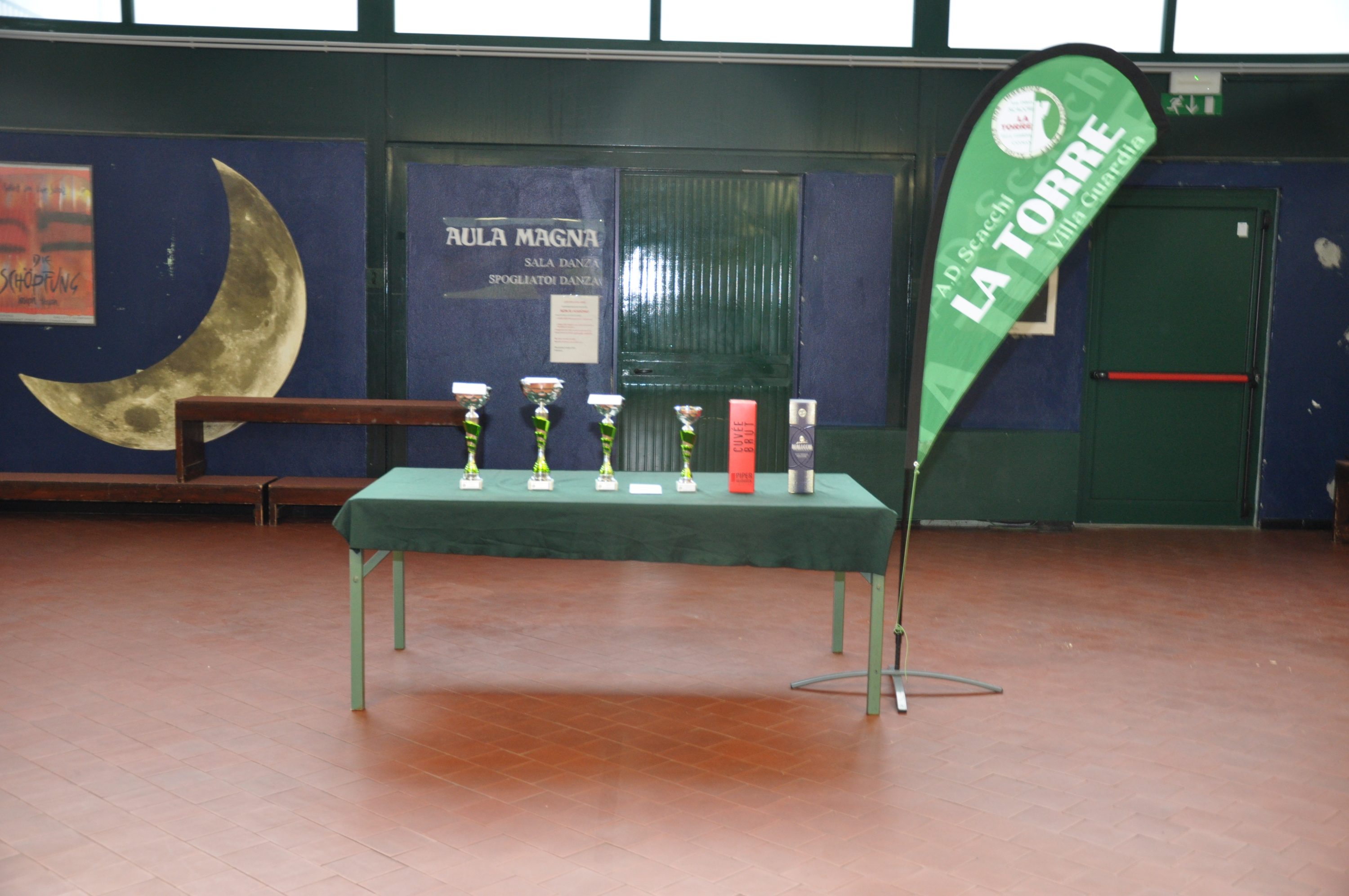 A table displaying several trophies and awards on a green tablecloth, with a green banner that reads 'LA TORRE' next to it, inside a decorated indoor space.