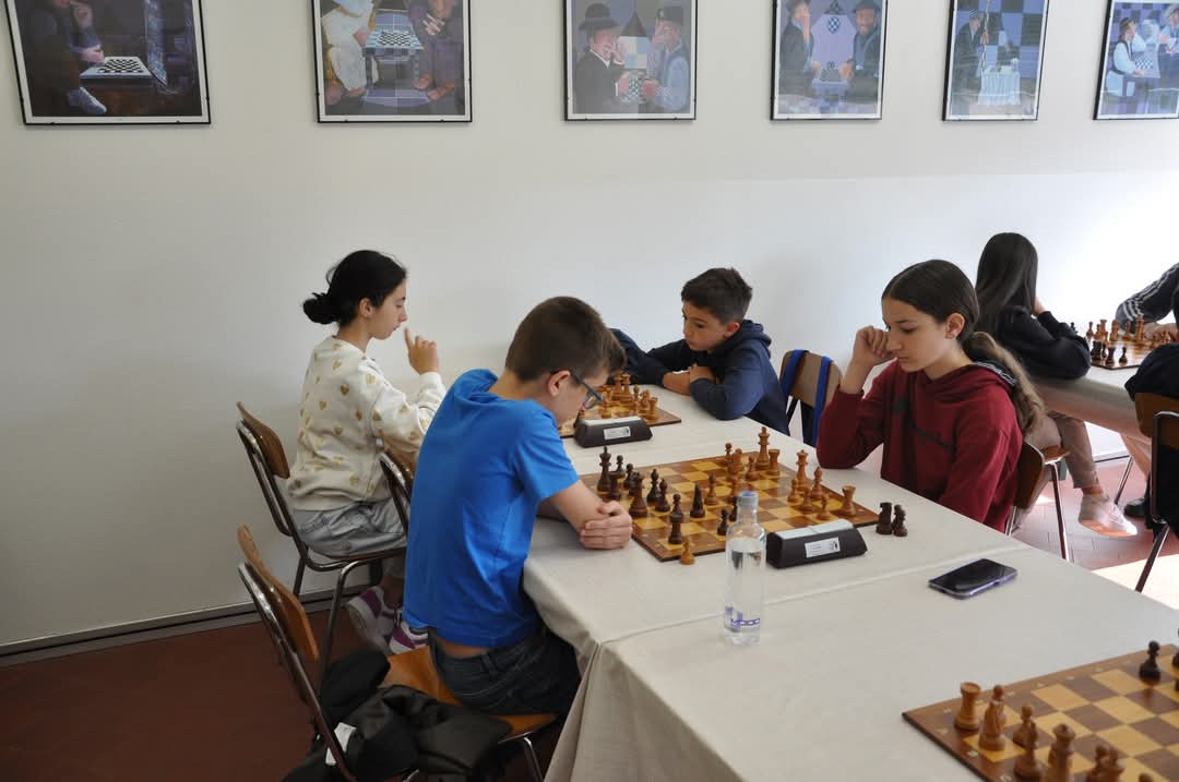 Giovani giocatori di scacchi concentrati durante una partita in un ambiente di torneo, con poster di scacchi appesi alle pareti.