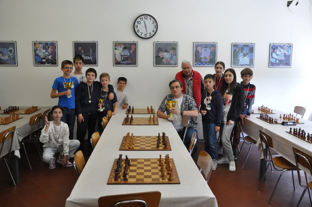 Gruppo di giovani giocatori di scacchi in una sala con tavoli e scacchiere, alcuni con trofei in mano.