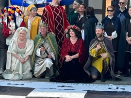 Group of individuals in medieval costumes, including kings and queens, posing together at an outdoor event.