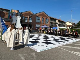 A large outdoor chessboard setup with people dressed in costumes attending an event in front of a building.