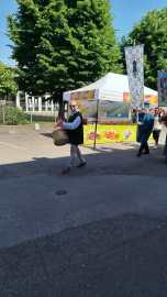 A person wearing a vest and carrying a basket walks past a colorful vendor tent under clear blue skies.