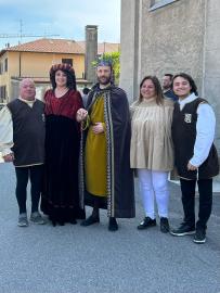 A group of five people dressed in historical costumes standing together on a street, with buildings in the background.