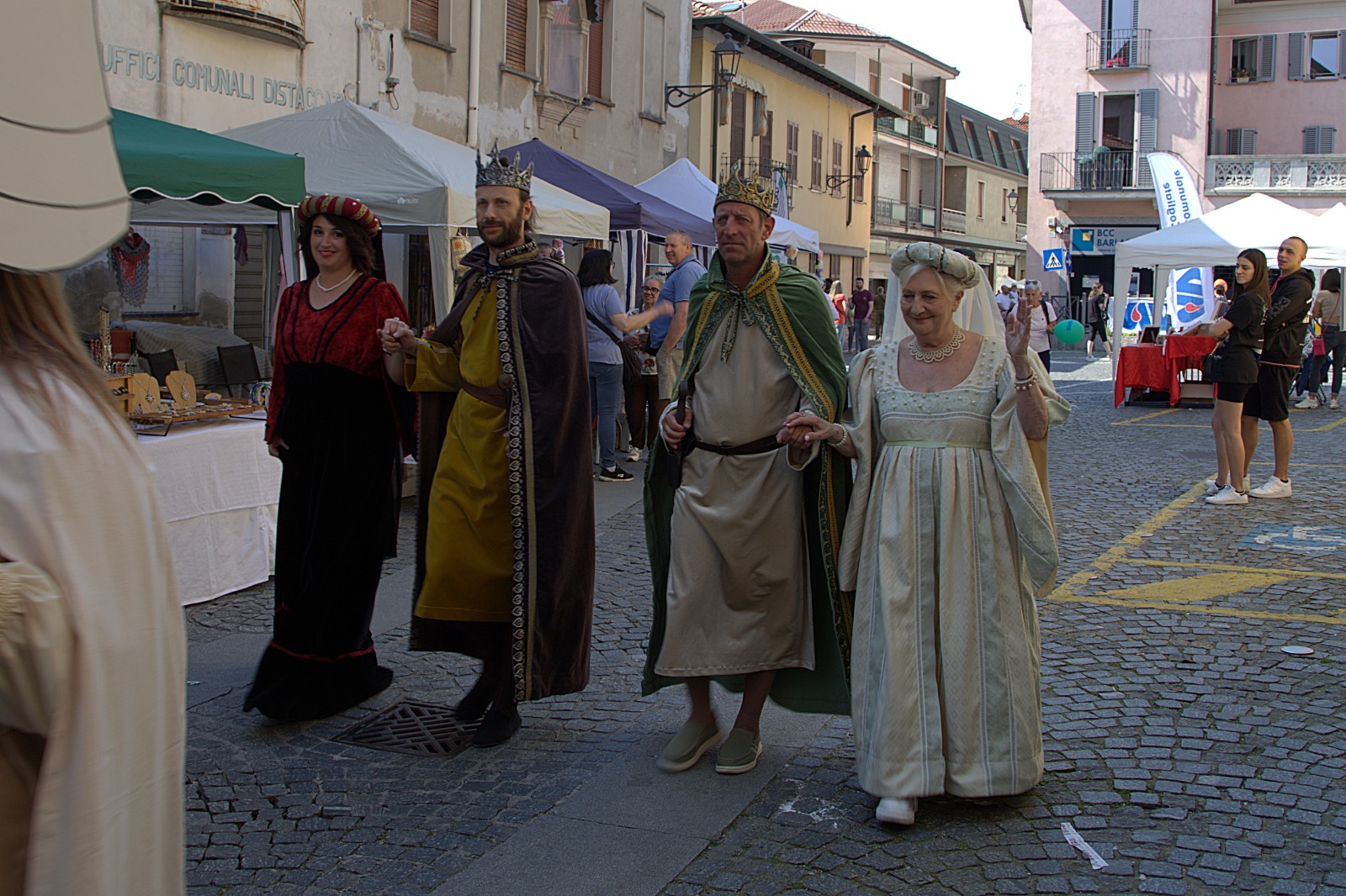 A group of four people in historical costumes walking down a cobblestone street during a festival.