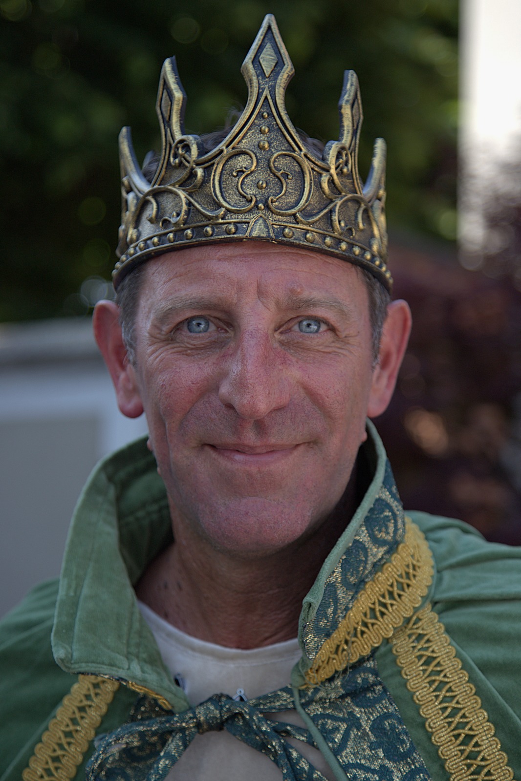 A man wearing a crown and a green cloak, smiling at the camera.