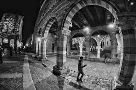 Black and white photo of a historic courtyard at night, featuring arched columns and illuminated buildings.