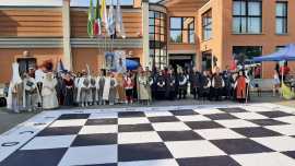 A group of people dressed in historical costumes gathered around a large checkered board in front of a building.