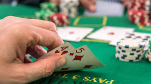 A hand holding playing cards displaying a five and a four of diamonds, with poker chips and a green felt table in the background.