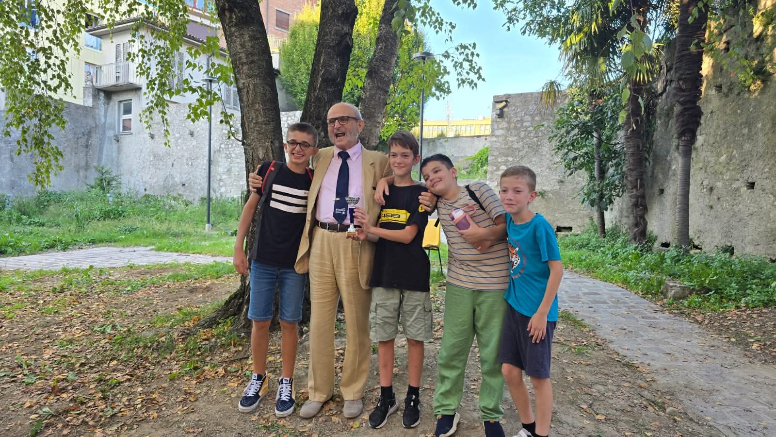 Un gruppo di cinque ragazzi posano insieme a un adulto in un parco, dietro di loro ci sono alberi e un'area verde.