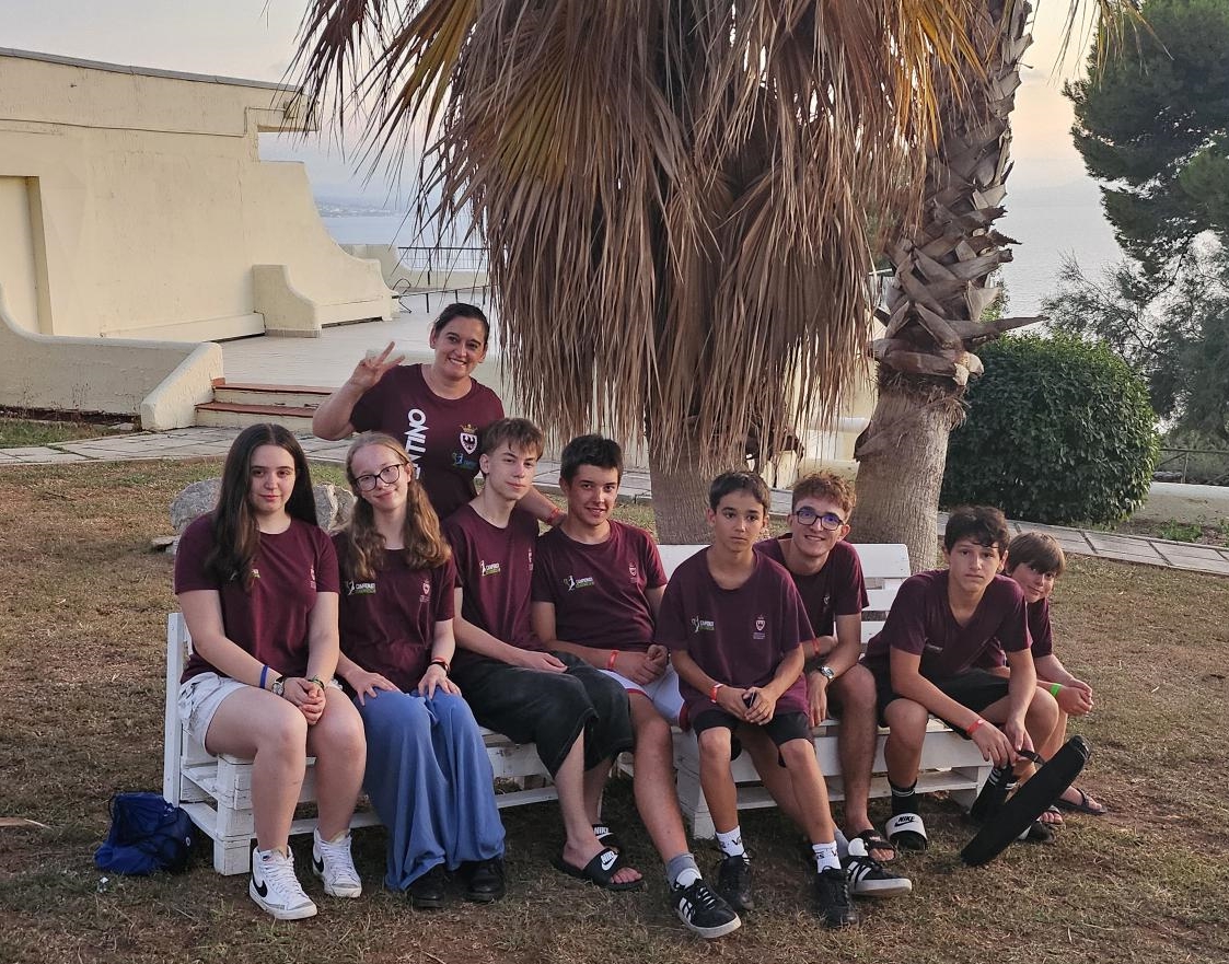 Un gruppo di giovani scacchisti sorridenti seduti su una panchina all'aperto, circondati da alberi, durante un evento o torneo di scacchi.