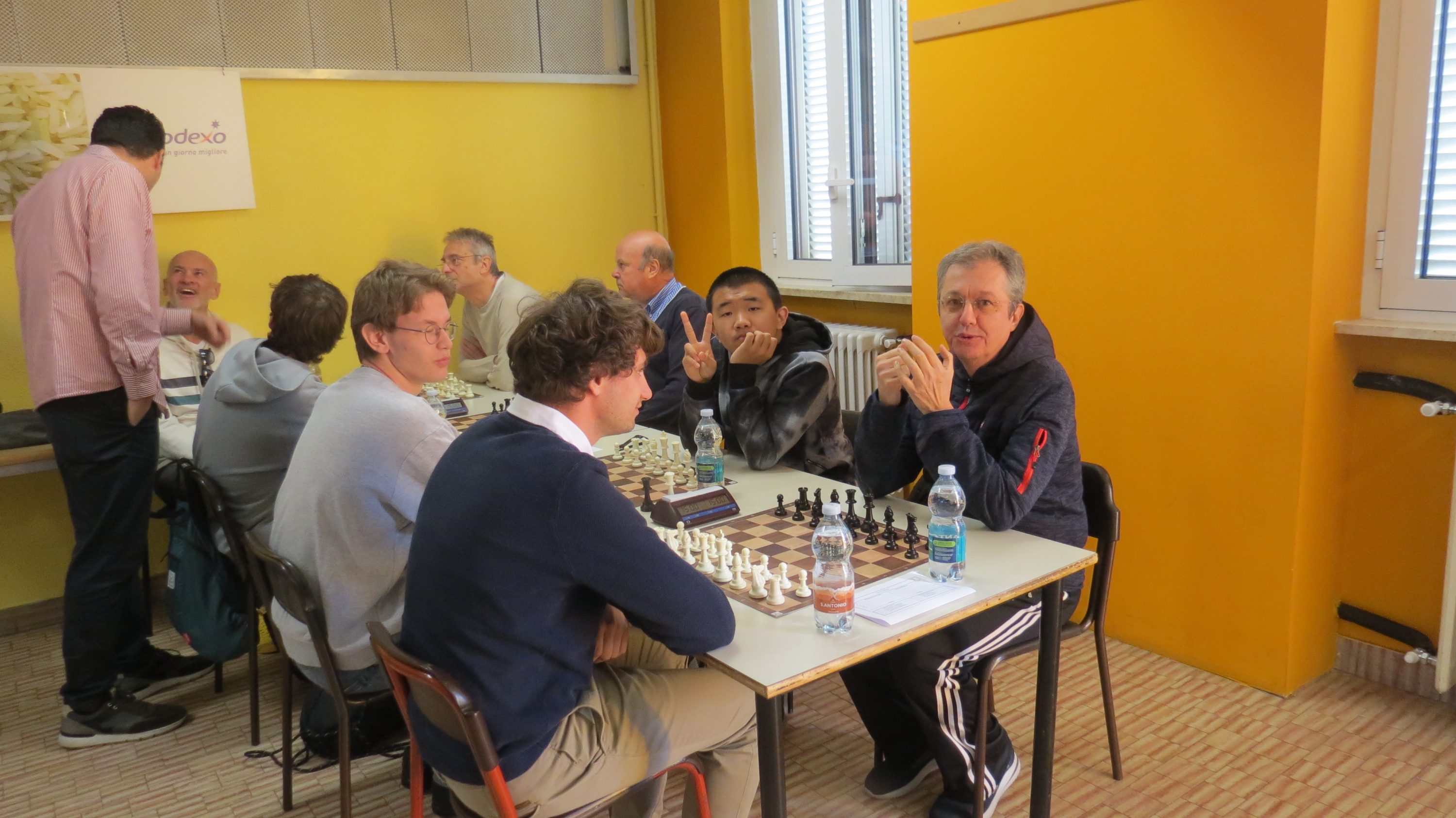Group of people playing chess at a table in a bright yellow room.