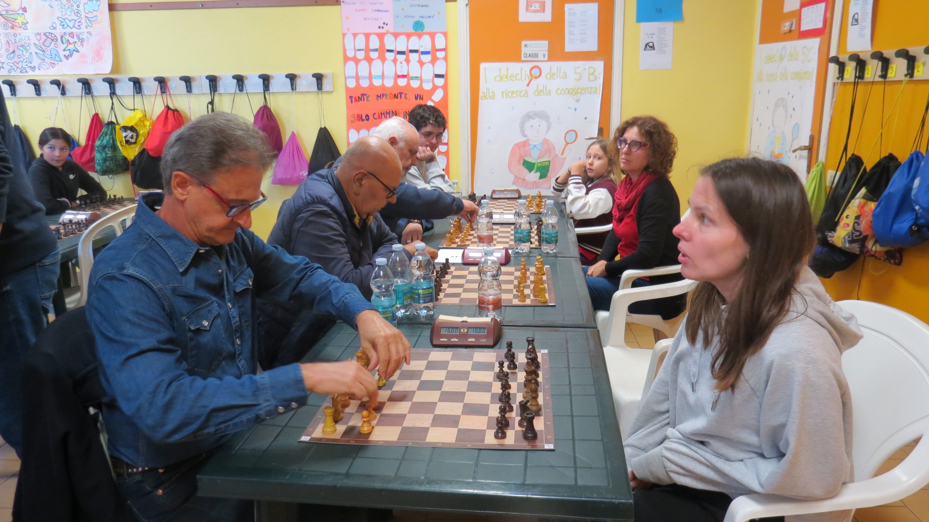 A group of people playing chess at a community center, with boards and pieces set up on tables.
