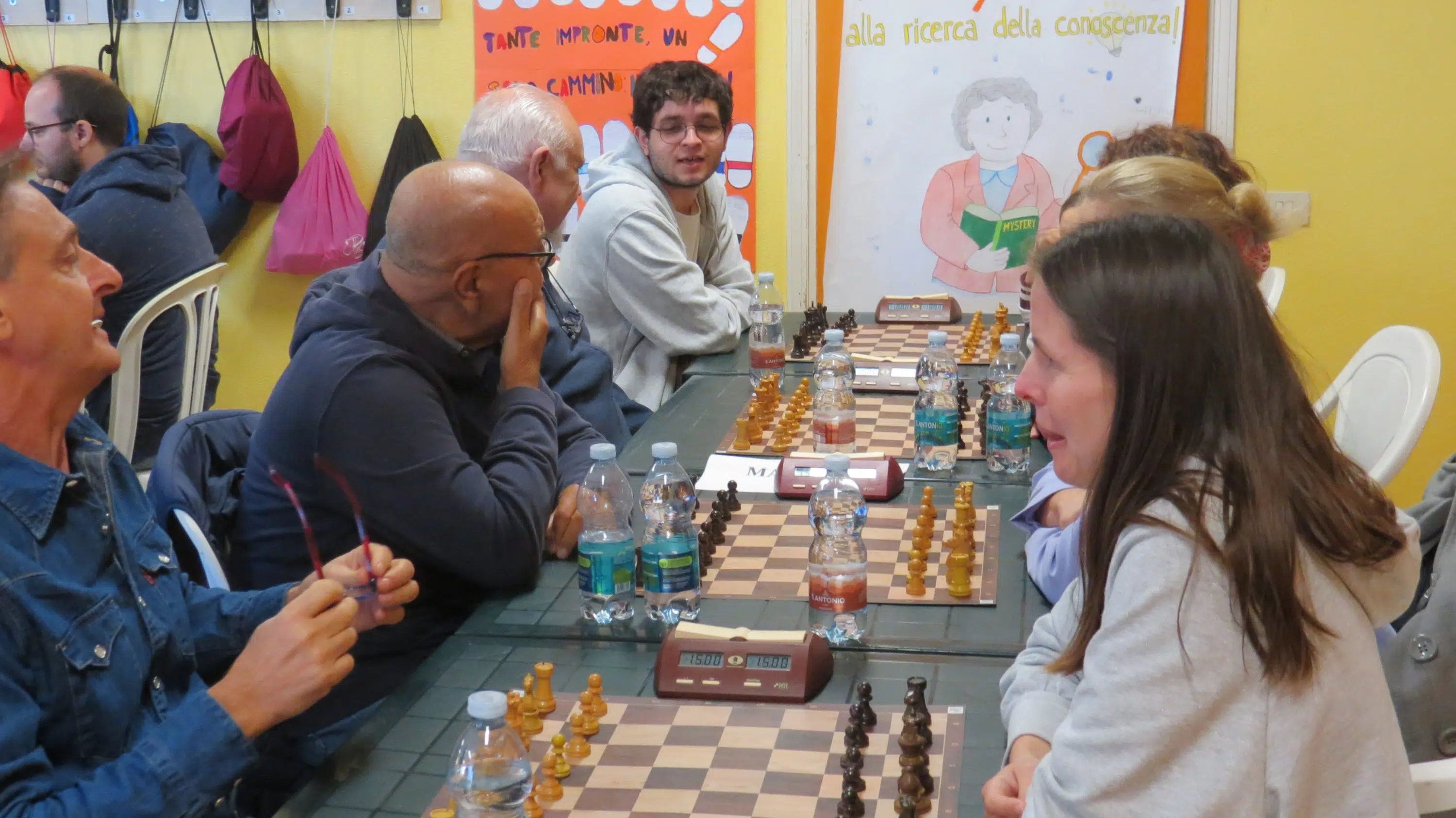 A group of people playing chess at a table with multiple chess boards and pieces, set in a colorful room.