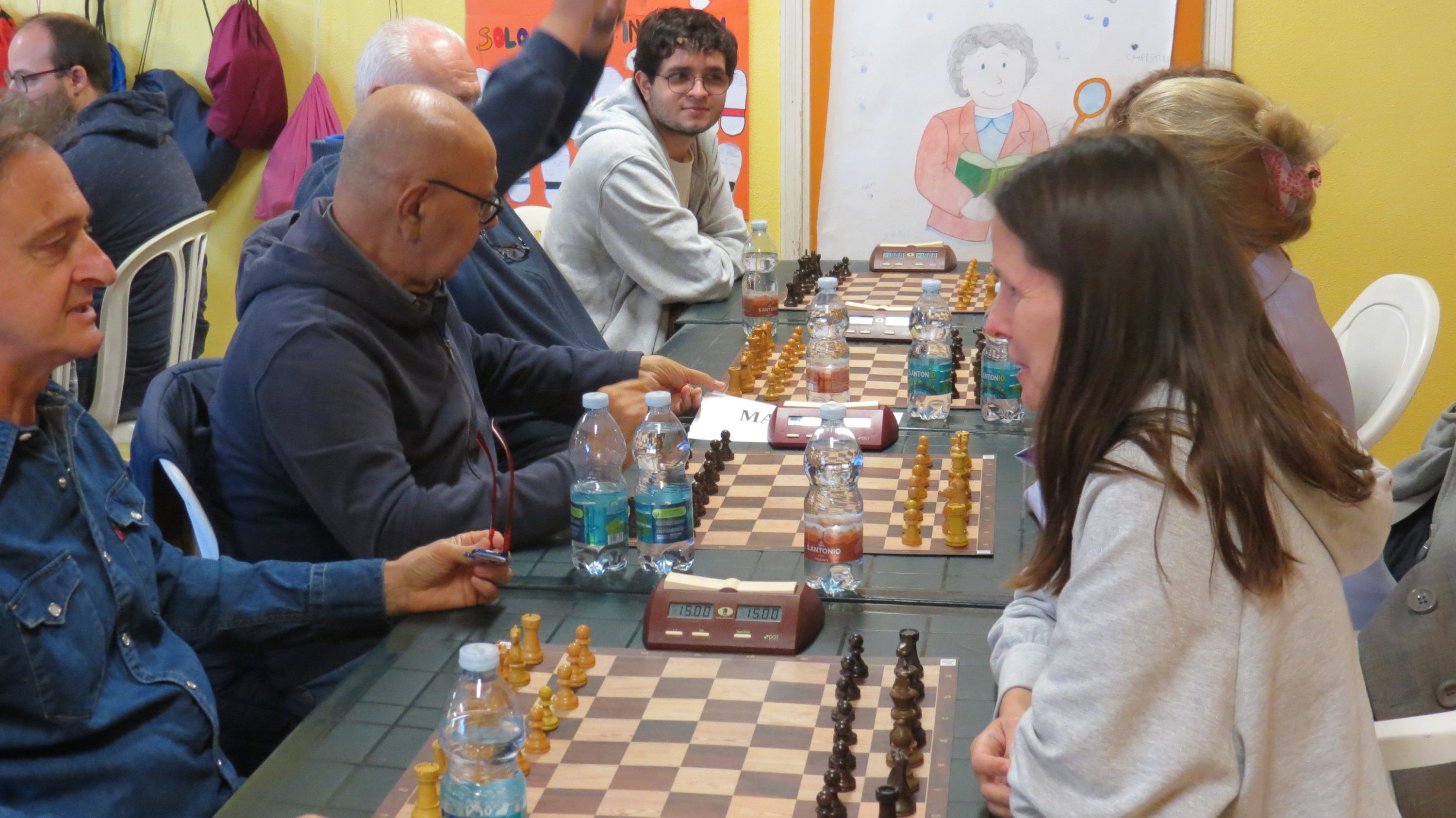 Un grupo de personas participando en un torneo de ajedrez, con tableros y piezas distribuidas sobre la mesa.