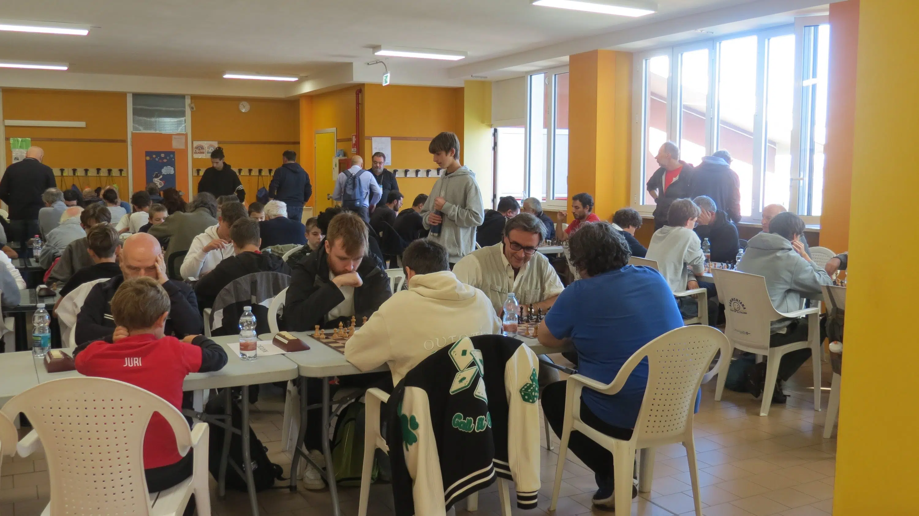 A busy indoor scene featuring multiple tables where people are engaged in activities, likely during a gaming or community event.