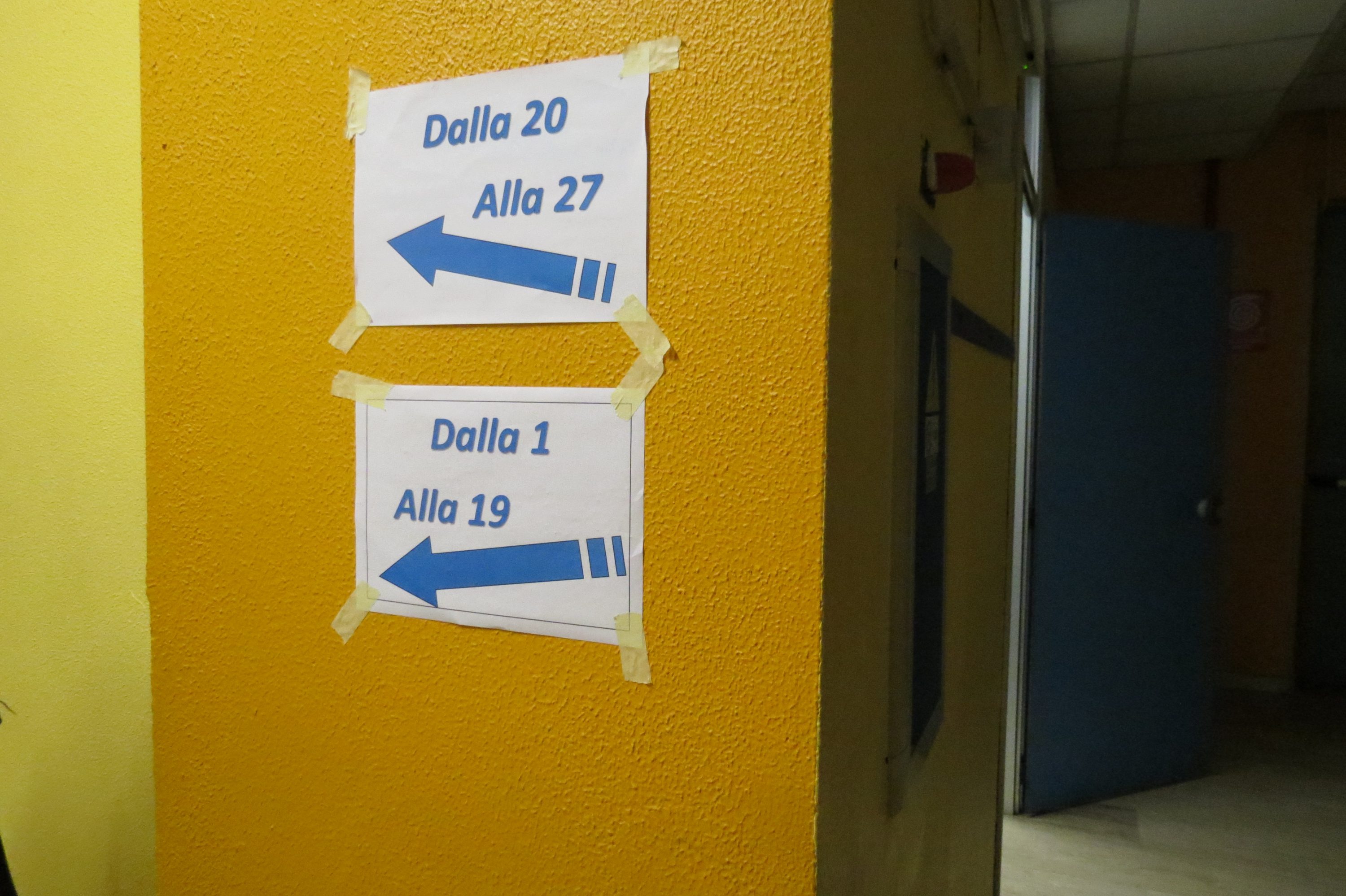 Due cartelli indicano le direzioni verso le stanze 20-27 e 1-19, appesi su un muro giallo.
