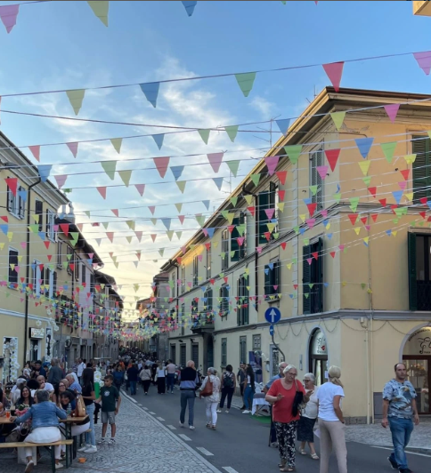 Strada principale di Binago, affollata di gente durante un evento organizzato dalla Pro Loco, con festoni colorati appesi sopra.