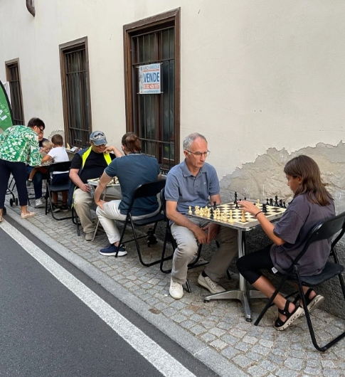 Persone sedute a tavoli all'aperto mentre giocano a scacchi, lungo una strada di Binago durante un evento della Pro Loco.