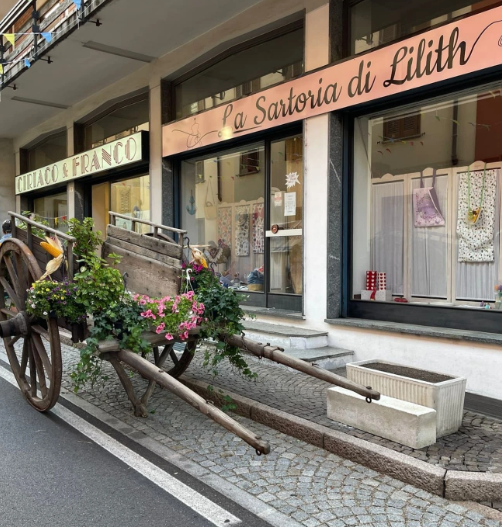 Carretto decorato con fiori posizionato davanti a una sartoria, in un ambiente urbano.