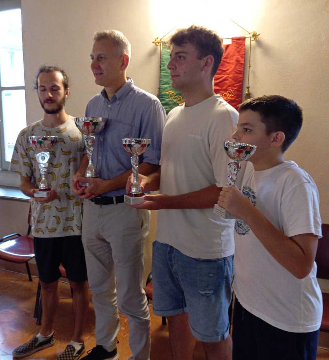 Quattro vincitori del Torneo Semilampo di scacchi, ognuno con un trofeo in mano, sorridono in un ambiente interno con decorazioni sportive.