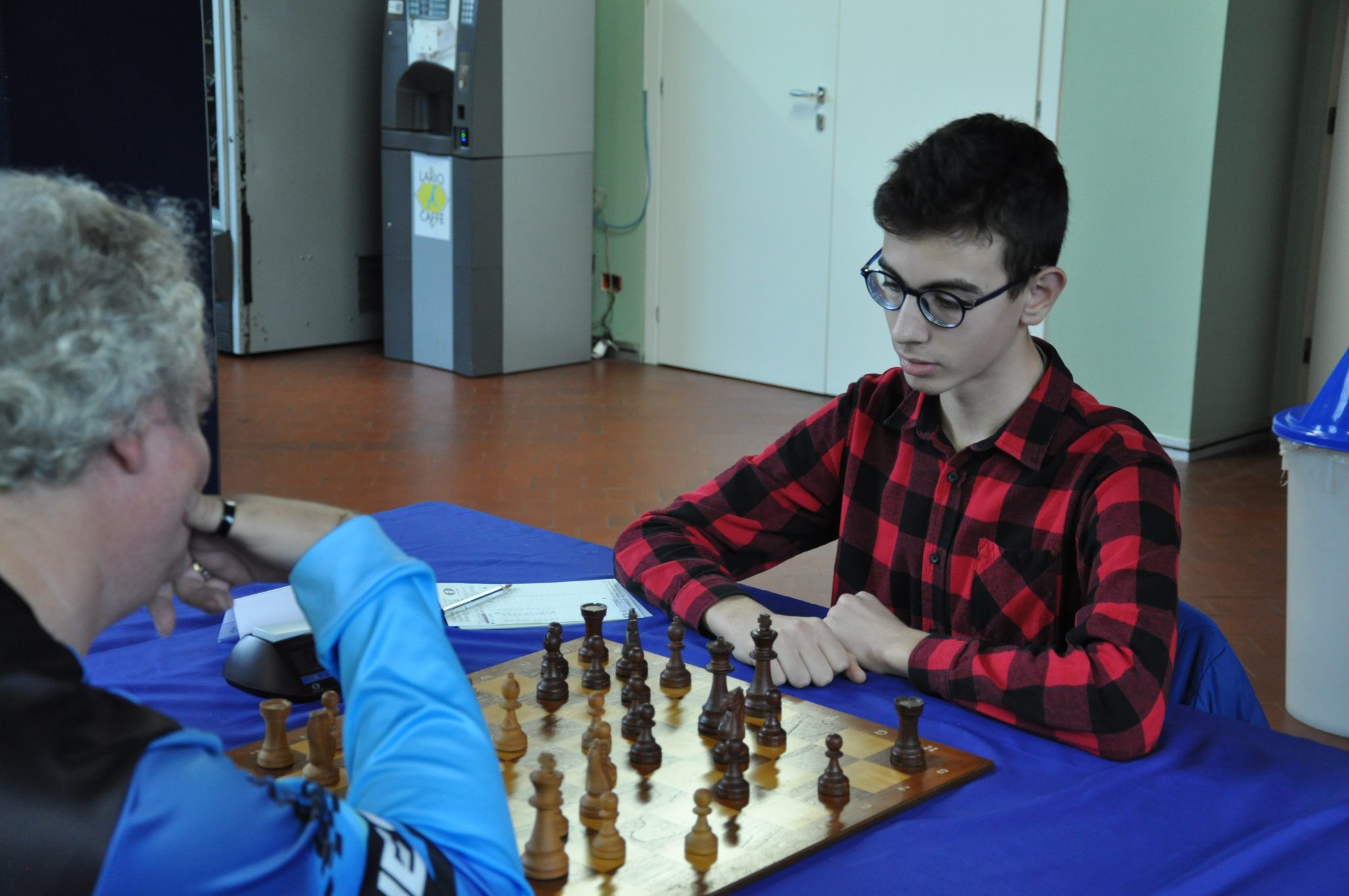 Two chess players engaged in a match, one wearing glasses and a plaid shirt, while the other is focused on their move.