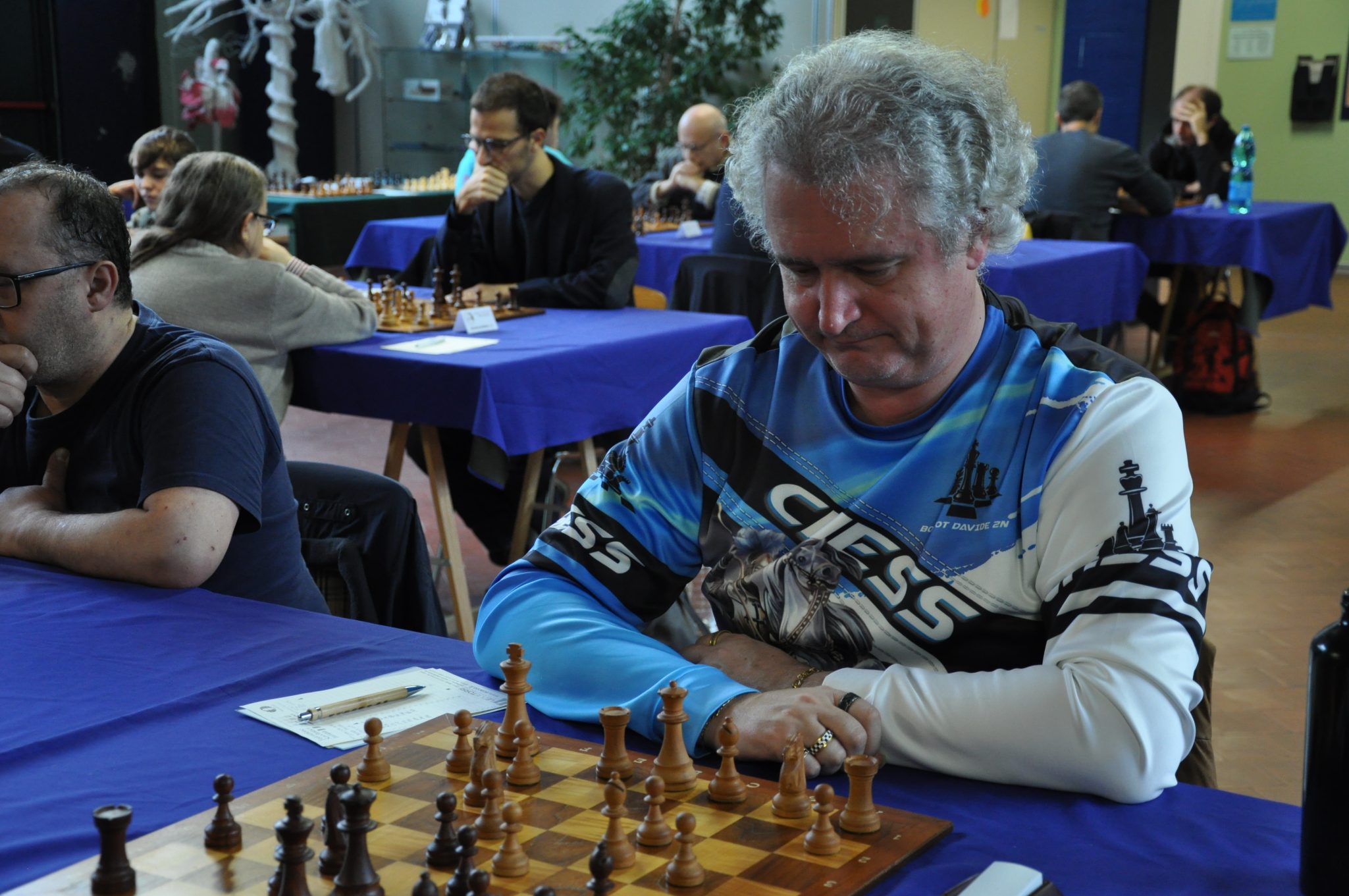 A man deep in thought while playing chess at a tournament, with a focused expression and a chessboard in front of him.