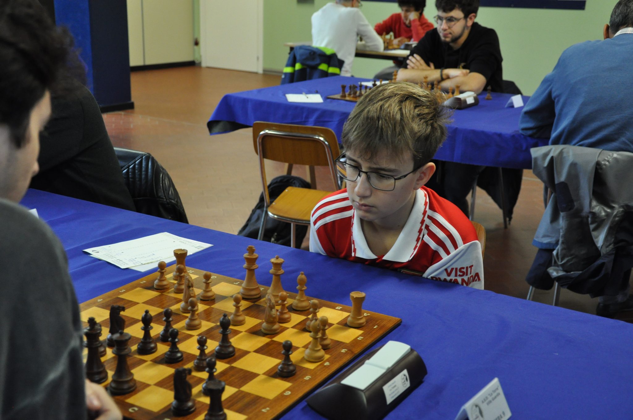 A young boy focused on a chess game during a tournament, with a chessboard and pieces in front of him.