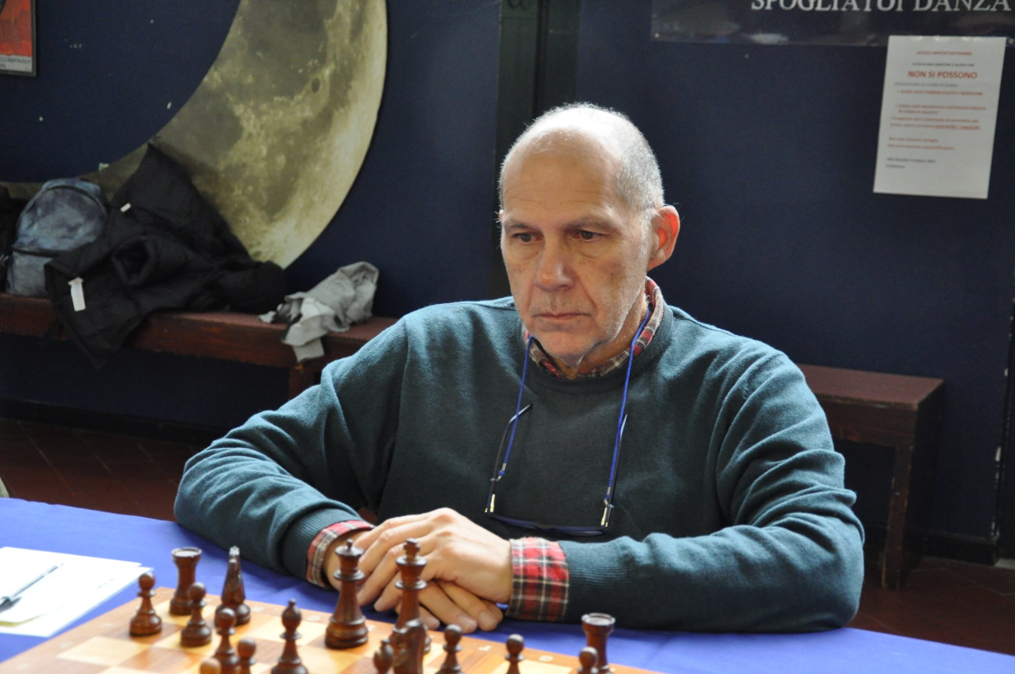 A focused man in a green sweater sitting at a chessboard with pieces arranged in front of him.